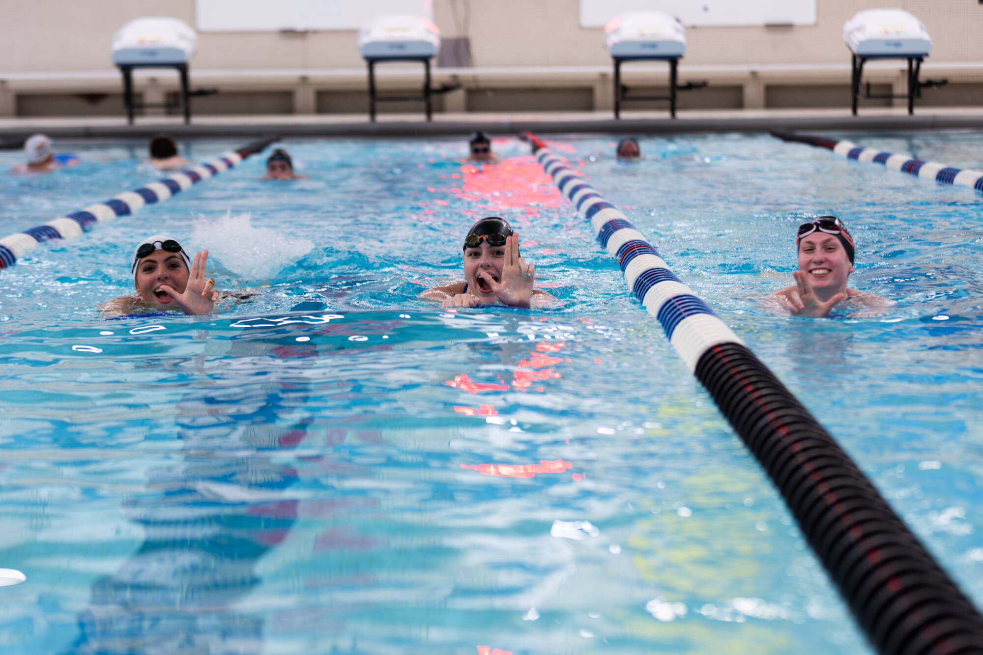 Three women kicking in the GVSU pool, doing the Anchor Up symbol